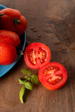 Tahta masadaki mavi tabakta olgun ve ıslak kırmızı domatesler.
