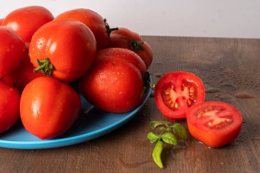 Tahta masadaki mavi tabakta olgun ve ıslak kırmızı domatesler.