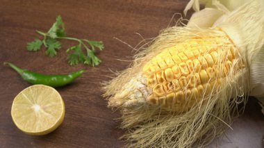 raw corn head with halved lemon fruit, parsley and green chili pepper on wooden background