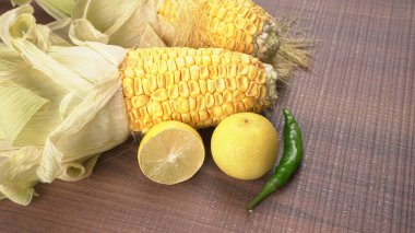 raw corn heads with lemon fruit and green chili pepper on wooden background