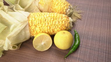 raw corn heads with lemon fruit and green chili pepper on wooden background