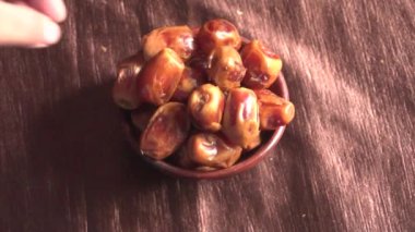 female hand take dried dates from the bowl on the wooden table