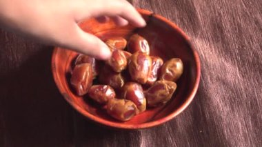 female hand take dried dates from the bowl on the wooden table