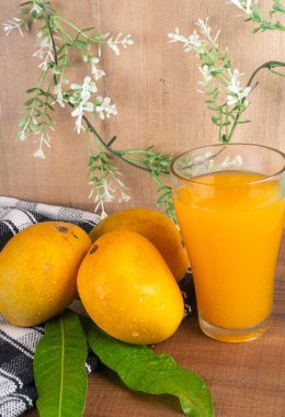 Tahta arka planda meyve suyu dolu olgun sarı mango meyvesi.