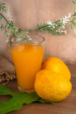 Tahta arka planda meyve suyu dolu olgun sarı mango meyvesi.