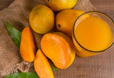 Tahta arka planda meyve suyu dolu olgun sarı mango meyvesi.