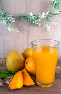 Tahta arka planda meyve suyu dolu olgun sarı mango meyvesi.