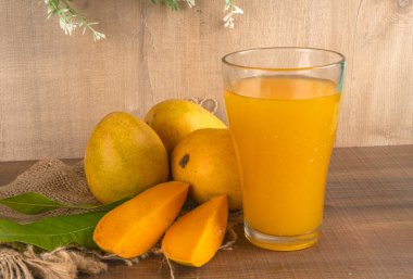 Tahta arka planda meyve suyu dolu olgun sarı mango meyvesi.