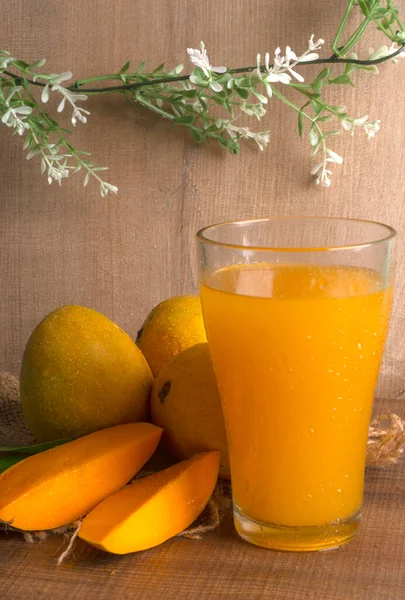 Tahta arka planda meyve suyu dolu olgun sarı mango meyvesi.