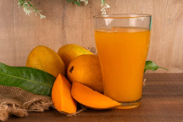 Tahta arka planda meyve suyu dolu olgun sarı mango meyvesi.