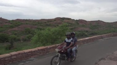 Kahverengi taşlı çitlerle antik yolda bisiklet süren insanlar.