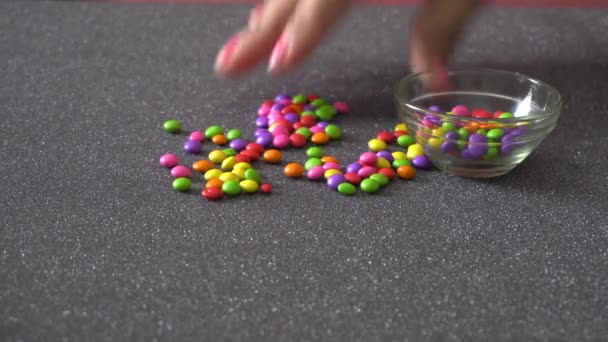 雌性手抓起并将彩色小糖果倒入灰色表面的碗中 — 图库视频影像