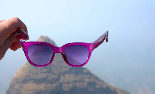 Female hand wearing sunglasses in mountains