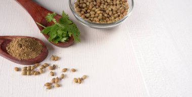 Kuru kişniş tohumları ile küçük bambu kaşıkları ve yeşil demet kişniş yaprakları, beyaz arka planda ünlü baharatlar.