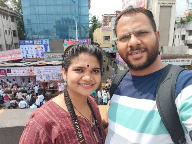 Pune, Maharashtra, India - 2 July 2024: Couple taking selfi during Pandharpur wari. Procession of Pilgrims marching towards Vitthala temple with singing religious songs with dancing. clipart