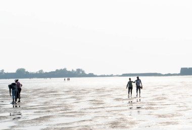 İnsanlar güneşli bir günde Hindistan 'da sahilde yürüyorlar.
