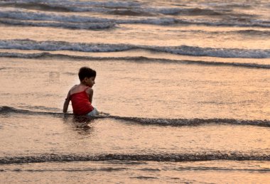 Gün batımında denizde yıkanan küçük çocuk.