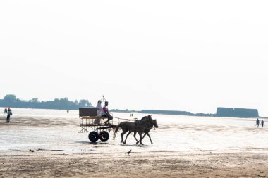 ALIBAG, MAHARASHTRA, INDIA - 25 Mart 2024: Kimliği belirsiz turistler sabah Kolaba Kalesi yakınlarındaki Alibag plajında iki tekerlekli bir arabaya biniyorlar.