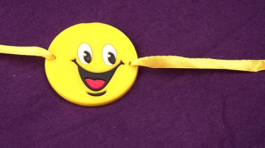 Geleneksel Hint Bracelet Rakhi mor arka planda, Rahibe Kravat Kardeşlerin Bileğinde Raksha Bandhan. Sarı gülümseyen emoji sembolü