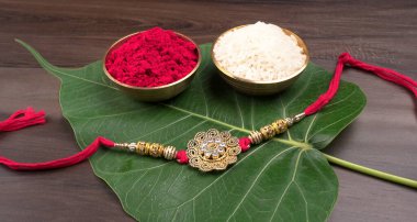 Traditional Indian Bracelet Rakhi, Sister Ties On Brothers Wrist on the Ocassion of Raksha bandhan. Bracelet, bowls of red powder and rice, fresh green leaf 