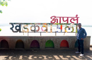 man posing near sign of Pune ki Chaupati, Khadakwasla Dam, Pune, India clipart