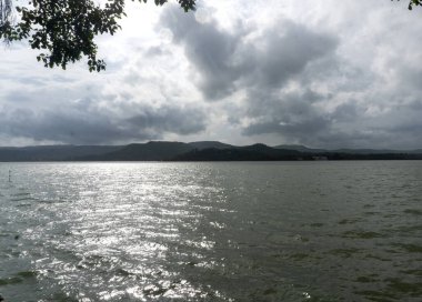 Dağlardaki gölün güzel manzarası, yeşil ağaçlar ve bulutlu gökyüzü. 