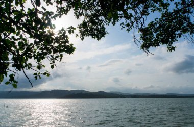 Dağlardaki gölün güzel manzarası, yeşil ağaçlar ve bulutlu gökyüzü. 