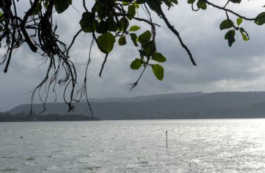 Dağlardaki gölün güzel manzarası, yeşil ağaçlar ve bulutlu gökyüzü. 