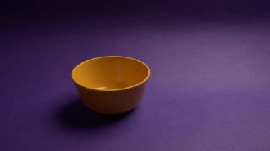 Mor zemin üzerinde sarı boş seramik kasenin yakın plan görüntüsü.                   