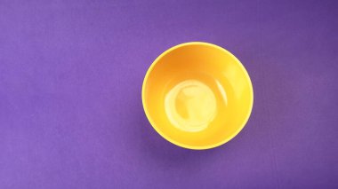 Mor zemin üzerinde sarı boş seramik kasenin yakın plan görüntüsü.                   