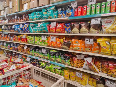 Pune, Maharashtra, Hindistan - 13 Ocak 2025; çok çeşitli gıda ürünleriyle dolu hareketli bir market koridoru. Süpermarketteki raflar satılmak üzere renkli paketlerle dolu..