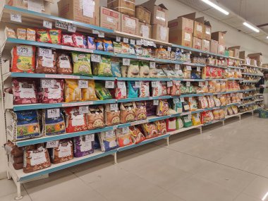 Pune, Maharashtra, Hindistan - 13 Ocak 2025; çok çeşitli gıda ürünleriyle dolu hareketli bir market koridoru. Süpermarketteki raflar satılmak üzere renkli paketlerle dolu..