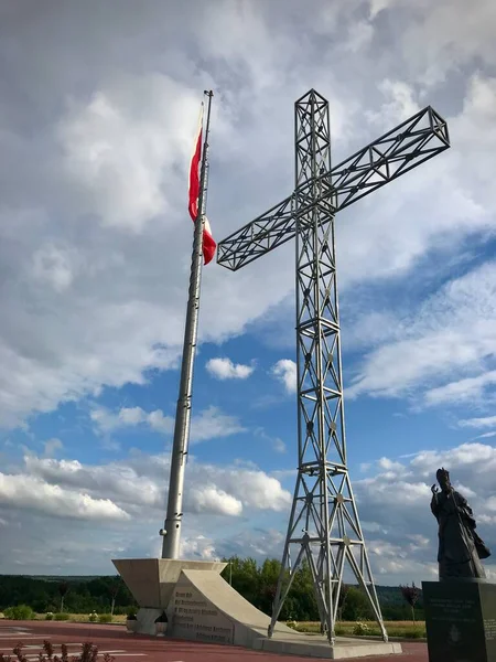 A statue and a cross on the hill, with a red and white Polish flag on the mast.