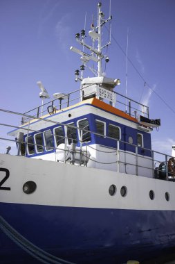 Yan tarafında 2 numara olan büyük mavi beyaz bir tekne. Tekne bir limanda park halinde.