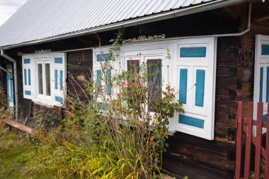 Önünde mavi ve beyaz panjurlar ve yeşil bir çalı olan bir ev. Ev eski ve kırsal bir havası var.