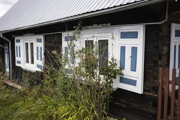 Önünde mavi ve beyaz panjurlar ve yeşil bir çalı olan bir ev. Ev eski ve kırsal bir havası var.