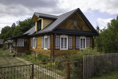 Kırmızı çitli ve beyaz çitli küçük bir ev. Evin bir sürü penceresi ve siyah bir çatısı var.