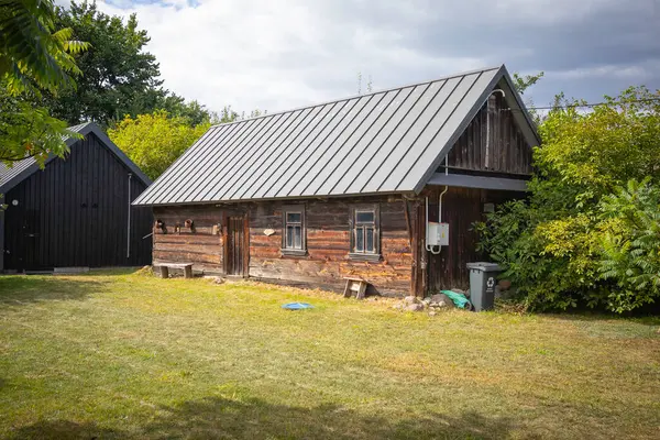 Önünde yeşil çöp kutusu olan küçük bir ev. Evin etrafı ağaçlarla çevrili ve kırsal bir hissi var.