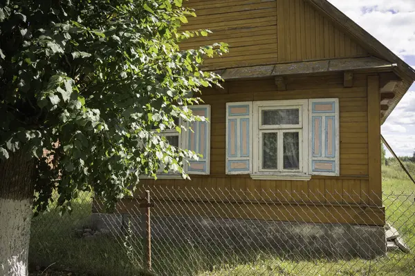 Beyaz çitli ve önünde ağaç olan küçük bir ev. Evin bir sürü penceresi ve verandası var.