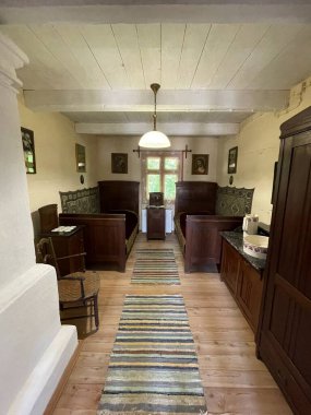 Ahşap zemini ve halısı olan küçük bir oda. Odada bir sandalye ve masa var.