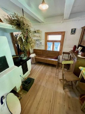 Küçük, sıcacık bir mutfak, ahşap zemin ve bir bank. Sobanın üstündeki duvarda asılı bir çelenk var.