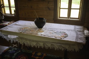Üzerinde beyaz bir masa örtüsü ve vazo olan bir masa. Masa örtüsünün dantel bir tasarımı var ve vazo siyah. Masa penceresi ve sandalyesi olan bir odada.