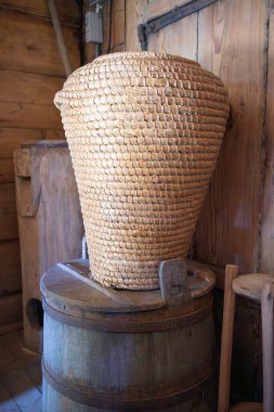 Samandan yapılmış büyük bir sepet varilin üzerinde duruyor. Sepet kahverengi ve kırsal bir görünüme sahip. Fıçı da kahverengi ve ahşap sapı var. Sahne rahat ve rustik bir hava veriyor.