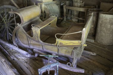 Yeşil saplı ahşap bir kızak diğer ahşap nesnelerle dolu bir odada oturuyor. Manzara nostaljik ve kırsal