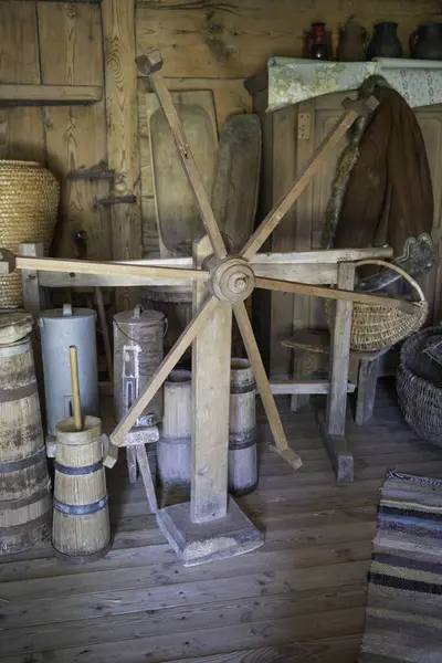 Ahşap bir tekerlek diğer ahşap nesnelerle dolu bir odada oturuyor. Odanın kırsal ve eski moda bir havası var.