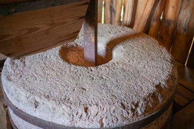 Büyük, eski moda tahta saplı öğütücü bir tekerlek kırsal bir ortamda oturur. Tekerlek taştan yapılmıştır ve direksiyonu çevirmek için kullanılan ahşap bir sapı vardır.