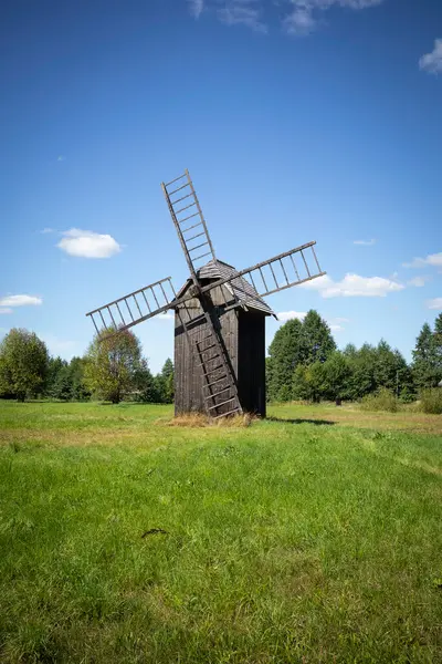 Bir yel değirmeni çim tarlasında duruyor. Gökyüzü açık ve mavi. Yel değirmeni eski ve bir merdiveni var.