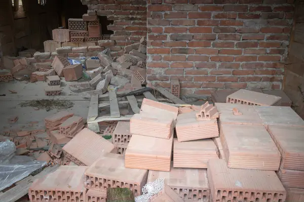 Bir odada tuğla ve moloz yığını. Tuğlalar yere ve duvara saçılmış. Sahne kaotik ve düzensiz.