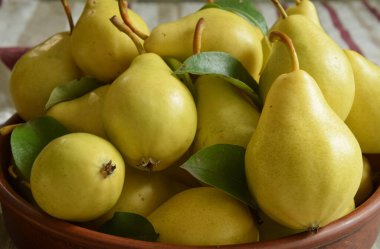 İçerideki ahşap masada kil kasede yeşil yapraklı olgun sarı armutlar. Mevsim hasadı. Pişirmek için taze malzemeler. Yemeye hazır tatlı meyveler. Durgun hayat. Önplana odaklan