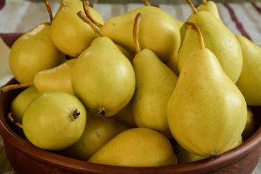 Kapalı alandaki ahşap masada kil kasede olgun sarı armutlar. Mevsim hasadı. Pişirmek için taze malzemeler. Yemeye hazır tatlı meyveler. Durgun hayat. Önplana odaklan